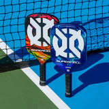 ONIX Supercell 22mm Pickleball Paddle, lifestyle photo, two paddles resting against a net on a light blue court
