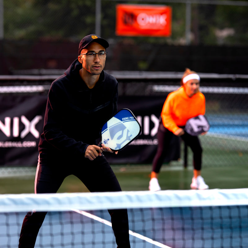 ONIX Composite Evoke Pro Pickleball Paddle, lifestyle photo, person close to the net in ready stance holding the paddle