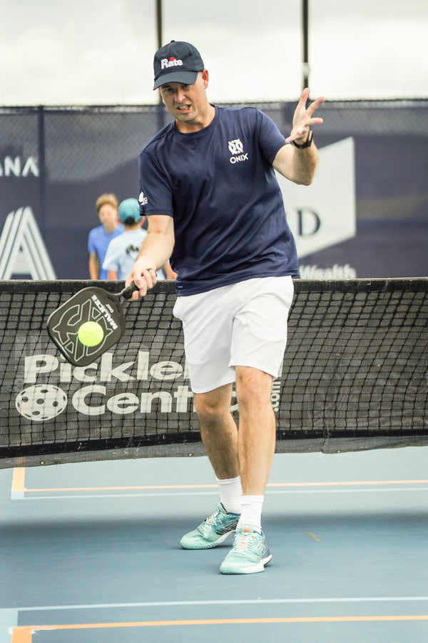 ONIX Malice DB Open Throat Raw Carbon Fiber Pickleball Paddle, lifestyle photo, player swinging and hitting a ball
