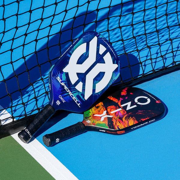 ONIX Supercell 22mm Pickleball Paddle, lifestyle photo, two paddles resting against the net on a light blue court